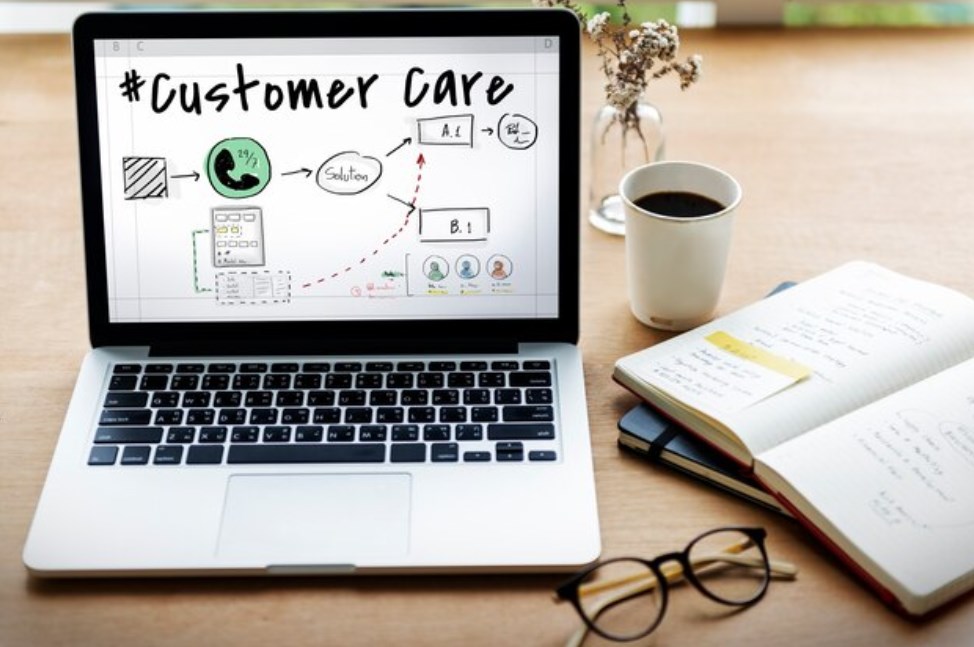 a laptop with the words “customer care” on the screen, glasses, a cup of coffee, and a notebook